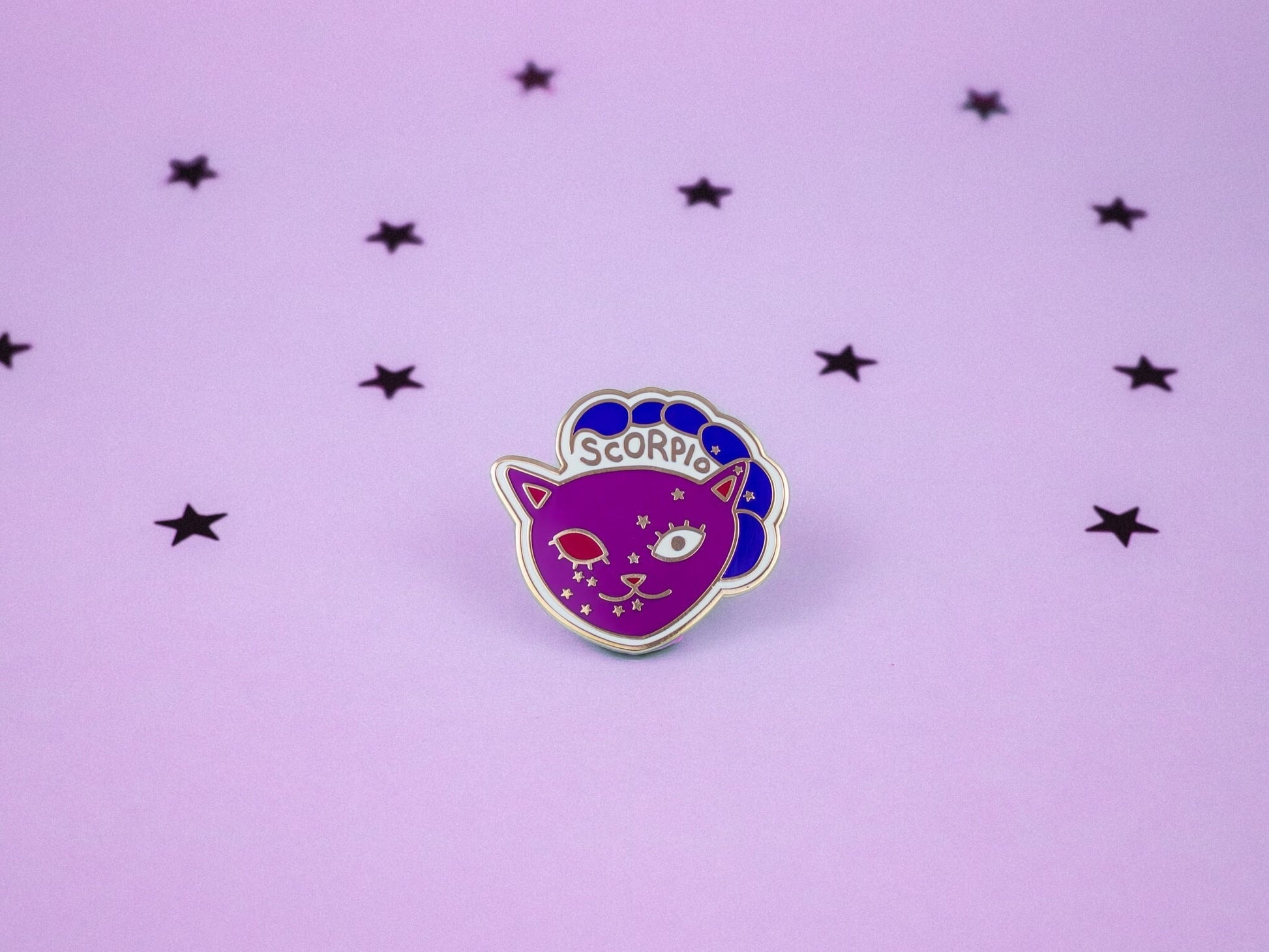 Scorpio cat enamel pin in purple and dark blue colour with a scorpion tail and scorpio constellation speckled across its face