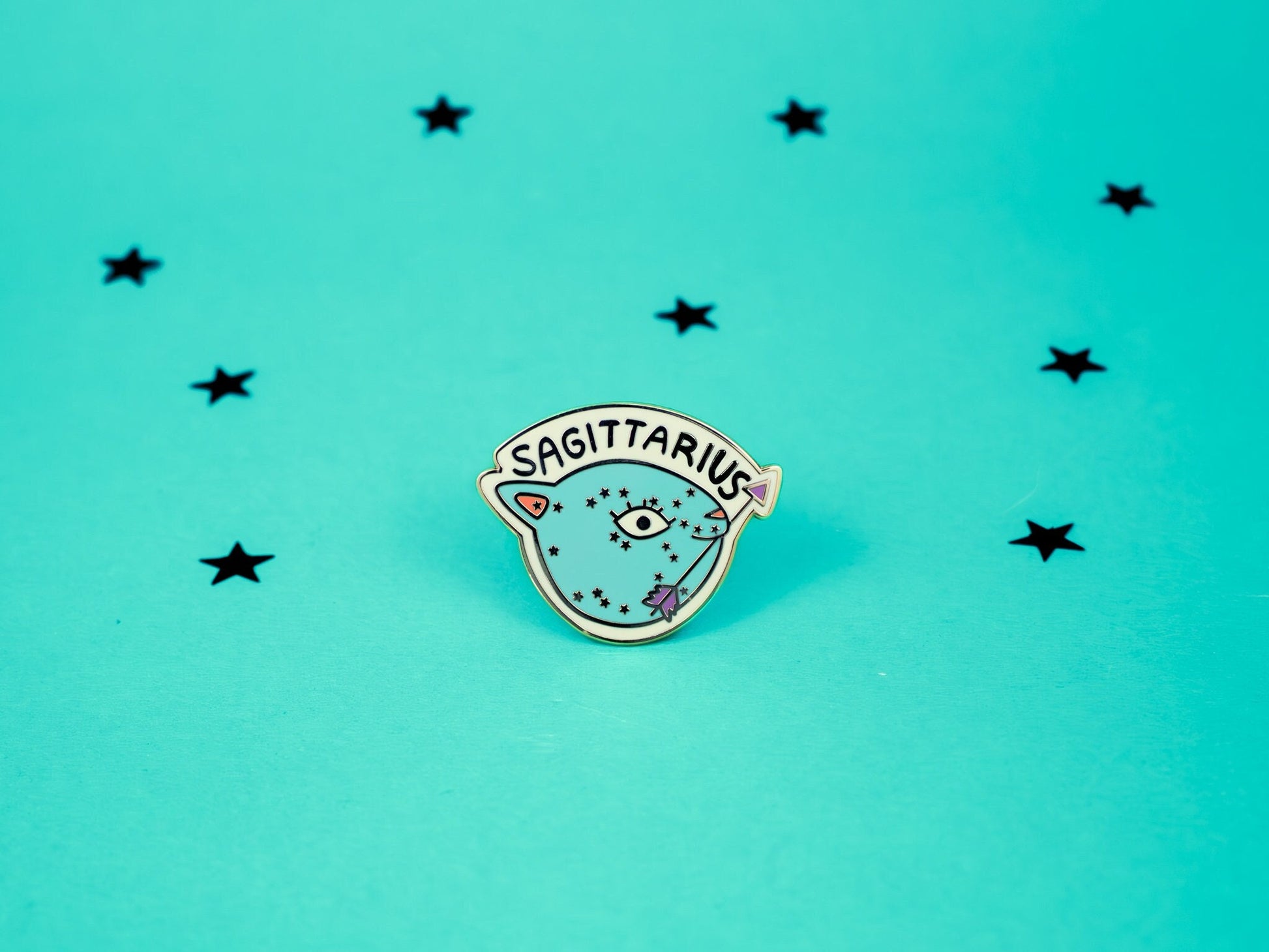 Sagittarius cat enamel pin in turquoise colour with an arrow in its mouth and sagittarius constellation speckled across its face.