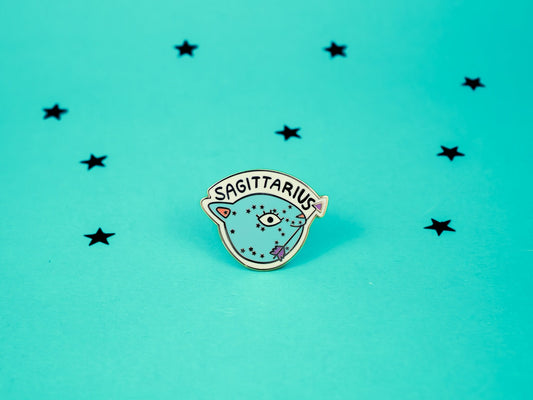 Sagittarius cat enamel pin in turquoise colour with an arrow in its mouth and sagittarius constellation speckled across its face.