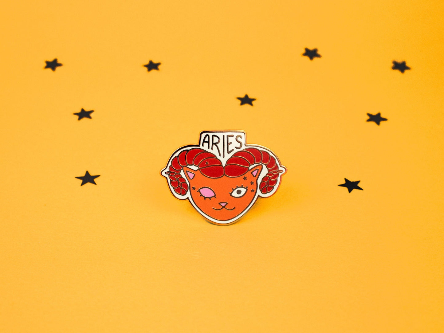 aries the ram cat enamel pin in orange and red colour with rams horns and aries constellation speckled across its face