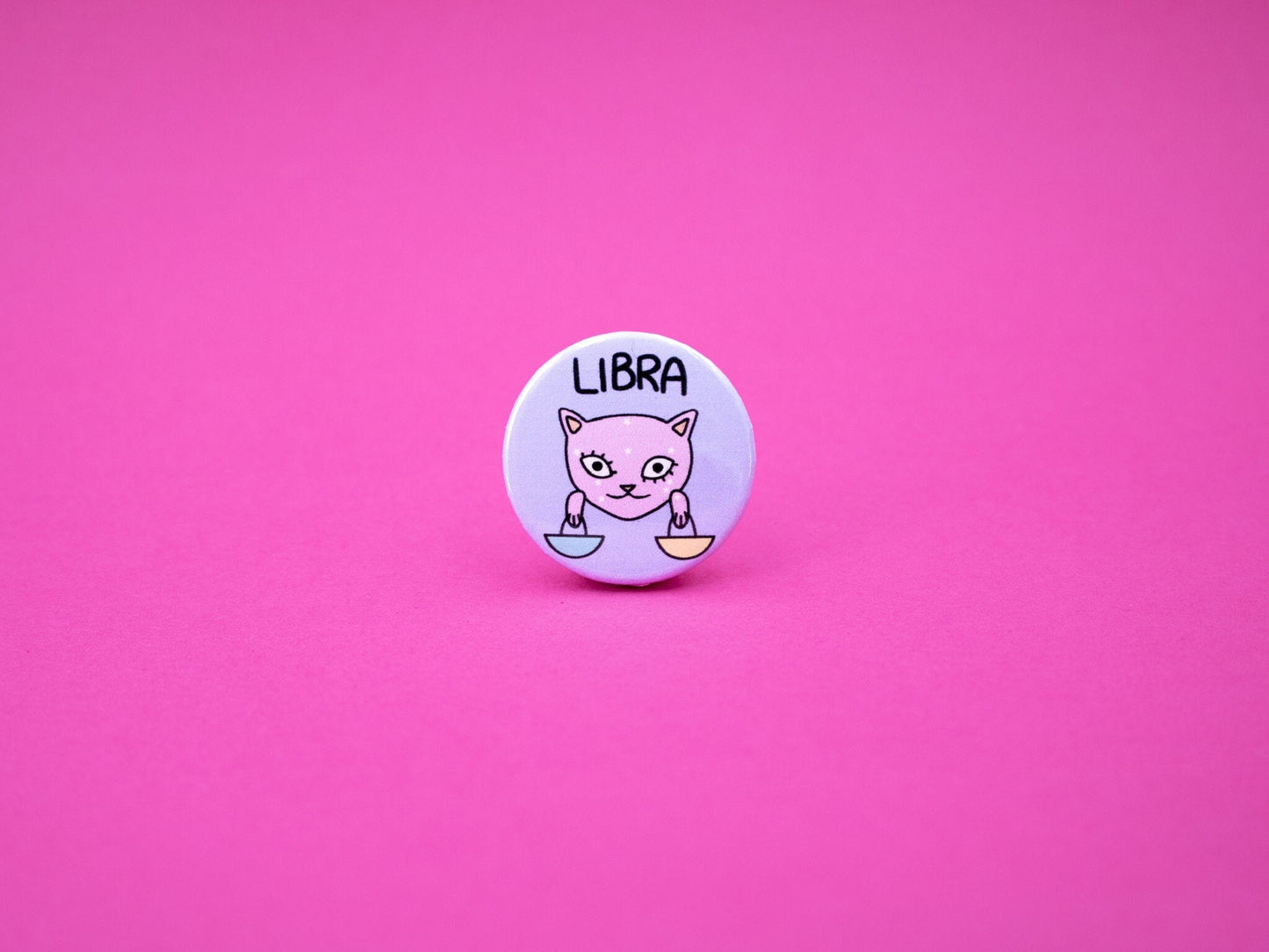 libra cat badge in pink and purple colours featuring a cat holding scales and the word &#39;LIBRA&#39; above