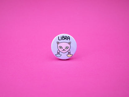 libra cat badge in pink and purple colours featuring a cat holding scales and the word &#39;LIBRA&#39; above