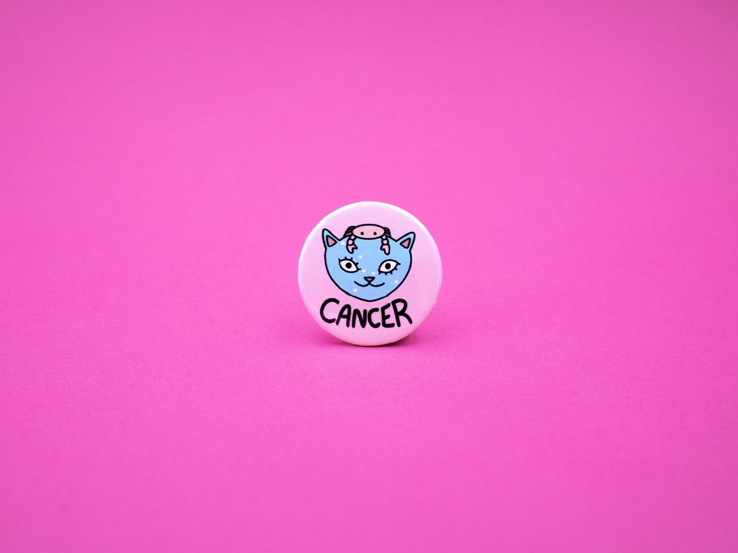 Pink button badge featuring a blue cat with small pink crab on its head to represent cancer zodiac and the word &#39;CANCER&#39; below