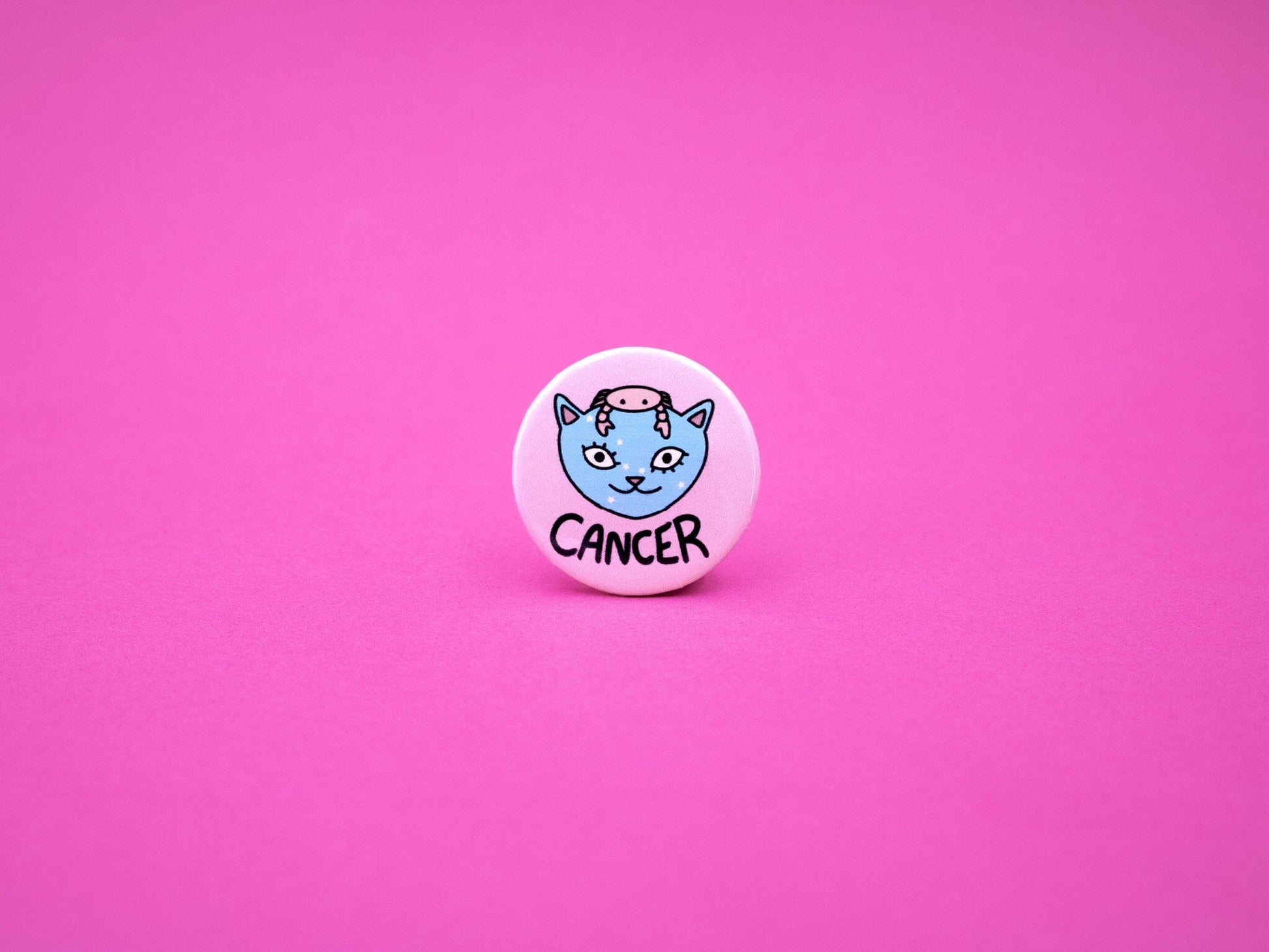 Pink button badge featuring a blue cat with small pink crab on its head to represent cancer zodiac and the word &#39;CANCER&#39; below